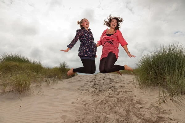 Two happy girls enjoying outdoor nature near the beach. Jumping in the air. Red and brown hair. Cloudy sky. — Stock Photo, Image