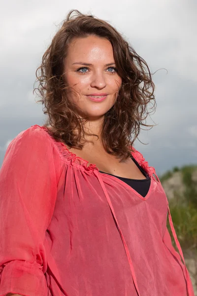 Šťastná mladá žena užívat přírody nedaleko pláže. hnědé vlasy. na sobě růžové tričko. zamračená obloha. — Stock fotografie