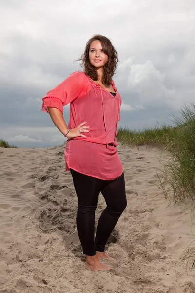 Joyeux jeune femme appréciant la nature en plein air près de la plage. Cheveux bruns. Elle porte une chemise rose. Ciel nuageux . — Photo