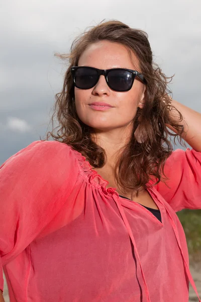 Gelukkig jonge vrouw genieten van buiten natuur in de buurt van het strand. bruin haar. het dragen van roze shirt en zwarte zonnebril. bewolkte hemel. — Stockfoto