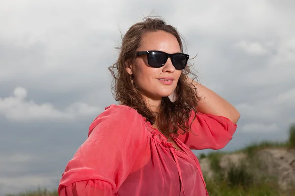 Счастливая молодая женщина, наслаждающаяся природой рядом с пляжем. Шатен. В розовой рубашке и черных солнечных очках. Облачное небо . — стоковое фото