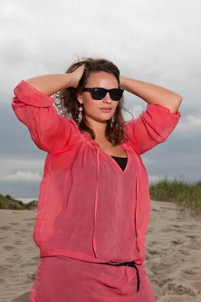 Mujer joven y feliz disfrutando de la naturaleza al aire libre cerca de la playa. Cabello castaño. Con camisa rosa y gafas de sol negras. Cielo nublado . —  Fotos de Stock
