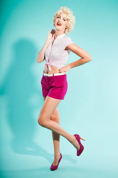 Sexy blondynka szałowy dziewczyna ubrana w różowy koszulkę i szorty. w stylu retro. studio mody strzał na białym tle na światło niebieskie tło. — Zdjęcie stockowe