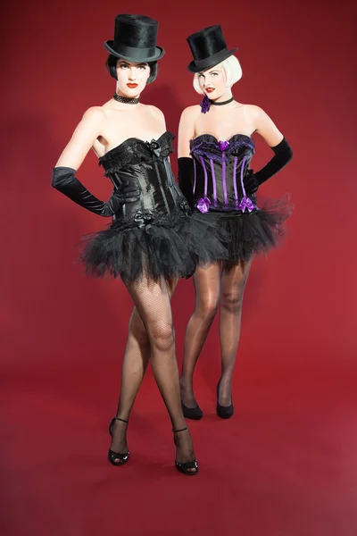 Dwa groteska szałowy kobiet z czarnymi włosami ubrany w kolorze fioletowym i czarnym. sexy stwarzają. czarnym kapeluszu. Studio mody strzał na białym tle na czerwonym tle. — Zdjęcie stockowe