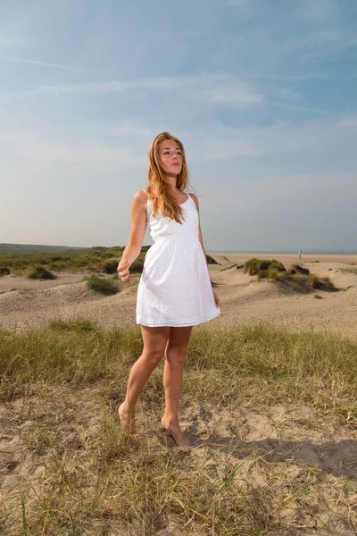 Bella ragazza con i capelli lunghi rossi indossando abito bianco godersi la natura vicino alla spiaggia. Caldo giorno d'estate con cielo nuvoloso blu . — Foto Stock