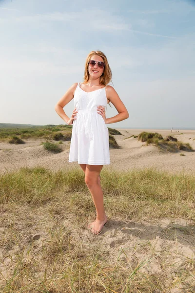Csinos lány visel fehér ruhát, és napszemüveg, élvezve a strand közelében, vörös hosszú haj. forró nyári napon a kék felhős ég. — Stock Fotó