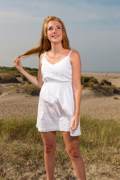 Pretty girl with red long hair wearing white dress enjoying nature near the beach. Hot summer day with blue cloudy sky. — Stock Photo, Image