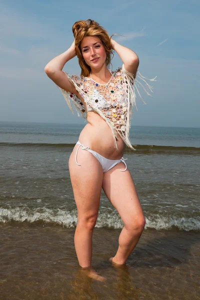 Красива дівчина з рудим довгим волоссям в білому бікіні насолоджується на відкритому повітрі на пляжі. Гарячий літній день з блакитним хмарним небом . — стокове фото