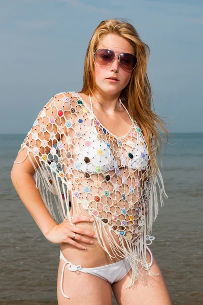 Jolie fille aux cheveux longs rouges portant un bikini blanc et des lunettes de soleil profitant de l'extérieur à la plage. Journée d'été chaude avec ciel nuageux bleu . — Photo