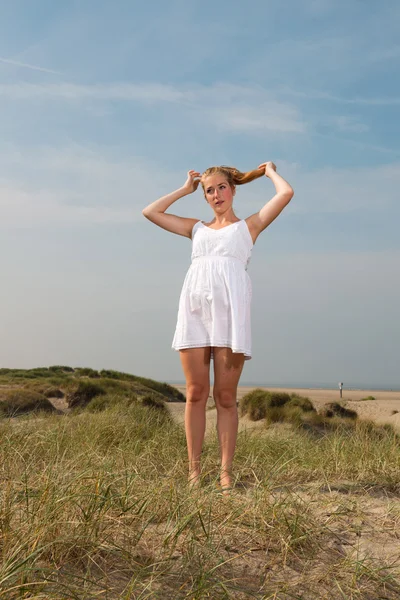 Hezká dívka s červenými dlouhé vlasy nosí bílé šaty užívat přírodu v blízkosti pláže. horký letní den s modré oblohy jasno. — Stock fotografie