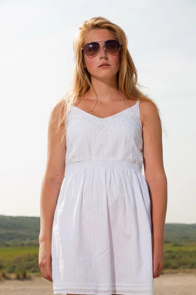 Beyaz elbise ve plaja yakın doğa güneş gözlüğü takmış kırmızı uzun saçlı güzel bir kız. sıcak yaz günü bulutlu gökyüzü mavi. — Stok fotoğraf
