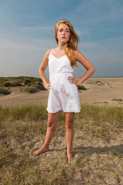 Красивая девушка с рыжими длинными волосами в белом платье наслаждается природой рядом с пляжем. Жаркий летний день с голубым облачным небом . — стоковое фото
