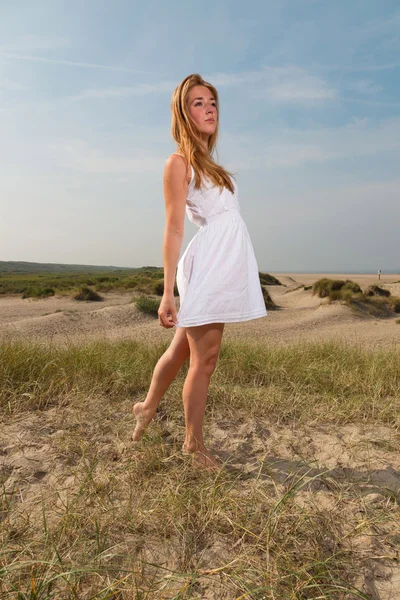 Hezká dívka s červenými dlouhé vlasy nosí bílé šaty užívat přírodu v blízkosti pláže. horký letní den s modré oblohy jasno. — Stock fotografie