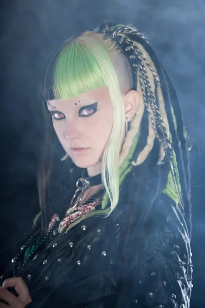 Menina punk cibernético com cabelo loiro verde e olhos vermelhos isolados em fundo preto com fumaça. Cara expressiva. Estúdio . — Fotografia de Stock