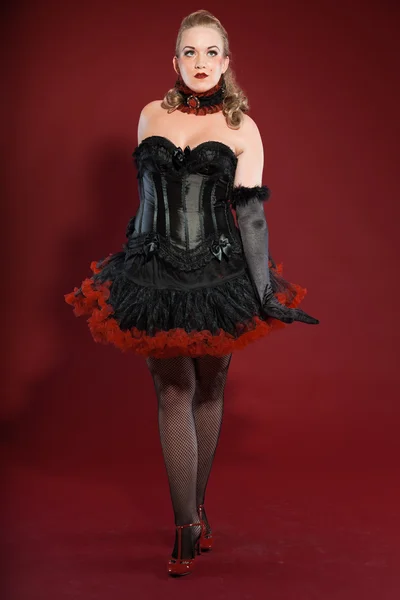 Sexy burlesque pin up femme aux longs cheveux blonds habillés en noir et rouge. Studio photo de mode isolé sur fond rouge . — Photo