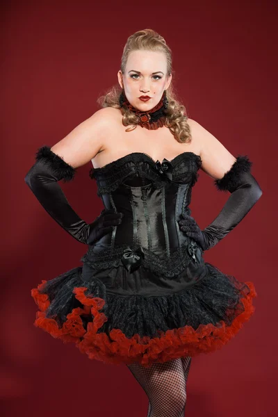Sexy burlesque pin up femme aux longs cheveux blonds habillés en noir et rouge. Studio photo de mode isolé sur fond rouge . — Photo