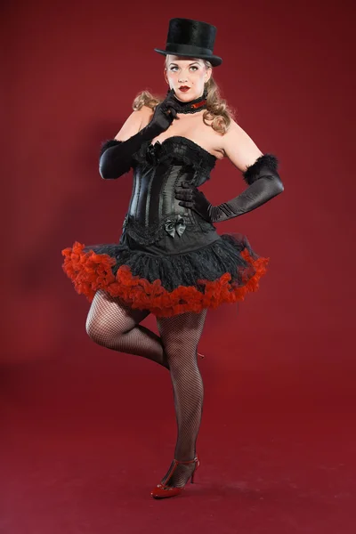 Sexy burlesque pin up woman with long blond hair dressed in black and red. Wearing black hat. Studio fashion shot isolated on red background. — Stock Photo, Image