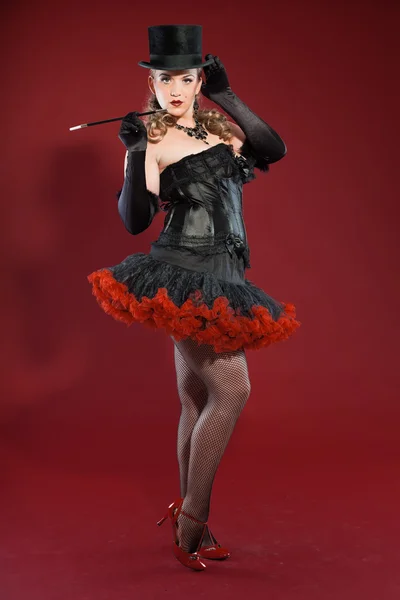 Σέξι παρωδίακο καρφίτσα μέχρι γυναίκα με μακριά ξανθά μαλλιά, ντυμένος με μαύρο και κόκκινο. Φορώντας μαύρο καπέλο και το κάπνισμα τσιγάρων. στούντιο μόδας πυροβόλησε απομονωμένες σε κόκκινο φόντο. — Φωτογραφία Αρχείου