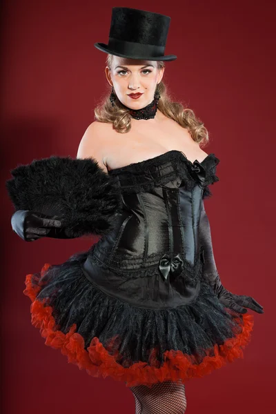 Σέξι παρωδίακο καρφίτσα μέχρι γυναίκα με μακριά ξανθά μαλλιά, ντυμένος με μαύρο και κόκκινο. Φορώντας μαύρο καπέλο. στούντιο μόδας πυροβόλησε απομονωμένες σε κόκκινο φόντο. — Φωτογραφία Αρχείου