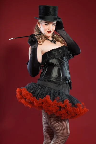 Sexy burlesque pin up woman with long blond hair dressed in black and red. Wearing black hat and smoking cigarette. Studio fashion shot isolated on red background. — Stock Photo, Image