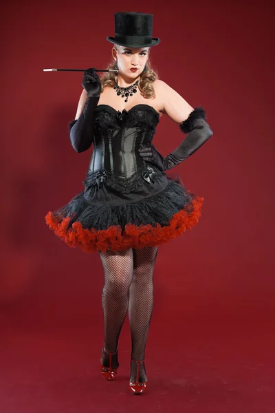 Sexy burlesque pin up donna con lunghi capelli biondi vestiti di nero e rosso. Indossava un cappello nero e fumava sigarette. Studio moda girato isolato su sfondo rosso . — Foto Stock