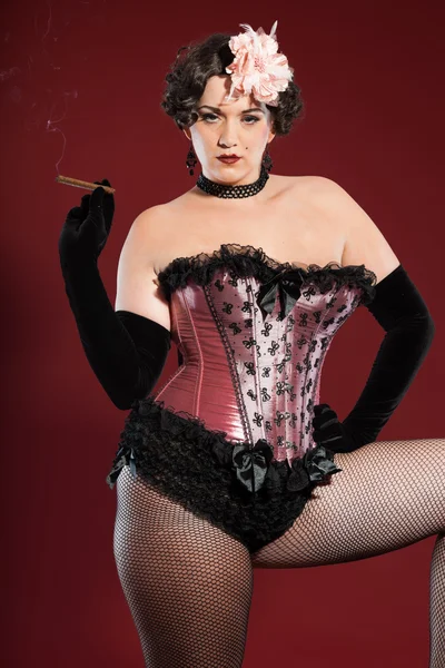 Sexy burlesque pin up donna con lunghi capelli biondi vestiti di rosa e nero. Sigaro fumante. Studio moda girato isolato su sfondo rosso . — Foto Stock