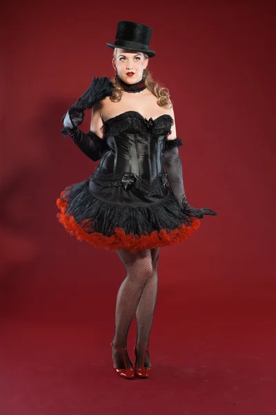 Sexy burleske pin-up vrouw met lang blond haar gekleed in zwart en rood. het dragen van zwarte hoed. Studio mode schot geïsoleerd op rode achtergrond. — Stockfoto