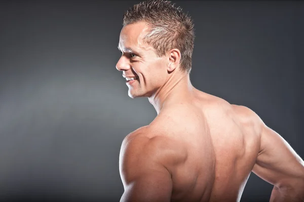 Shirtless muscled fitness man showing his back. Cool looking. Tough guy. Blue eyes. Blond short hair. Wearing black sunglasses. Tanned skin. Studio shot isolated on grey background. — Stock Photo, Image