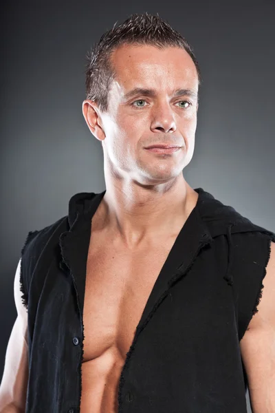 Muscled fitness man. Cool looking. Tough guy. Blue eyes. Blond short hair. Wearing black shirt. Tanned skin. Studio shot isolated on grey background. — Stock Photo, Image