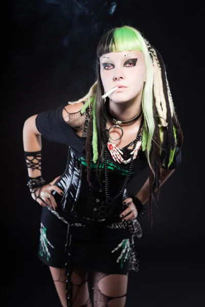 Cyber-Punk-Mädchen mit grün-blonden Haaren und roten Augen auf schwarzem Hintergrund. Gesichtsausdruck. Zigarette rauchen. Studioaufnahme. — Stockfoto