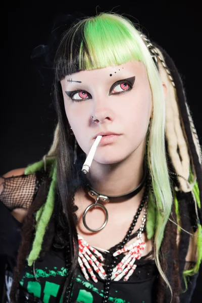 Cyber punk girl with green blond hair and red eyes isolated on black background. Expressive face. Smoking a cigarette. Studio shot. — Stock Photo, Image