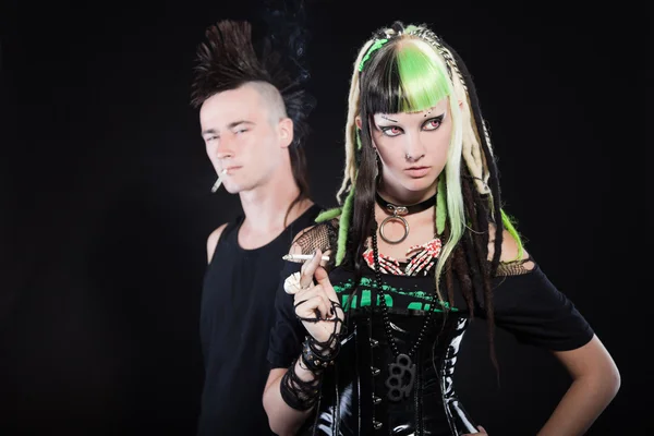 Couple of cyber punk girl with green blond hair and punk man with mohawk haircut. Expressive faces. Smoking cigarette. Isolated on black background. Studio shot. — Stock Photo, Image