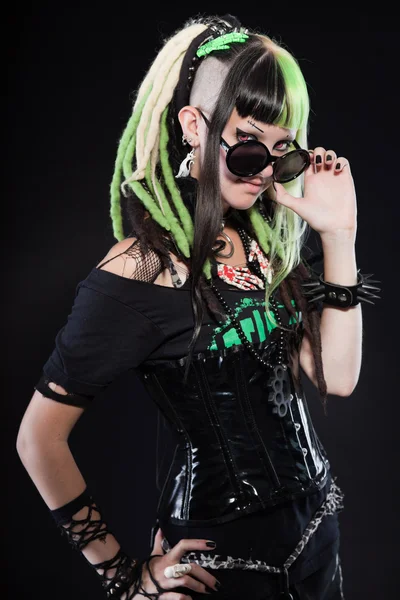 Cyber punk girl with green blond hair and red eyes isolated on black background. Wearing black sunglasses. Expressive face. Studio shot. — Stock Photo, Image