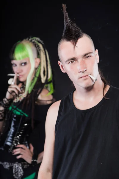 Pár cyber punk dívka s zeleným blond vlasy a punková muže s mohawk účesem. expresivní tváří. kouření cigaret. izolované na černém pozadí. Studio záběr. — Stock fotografie