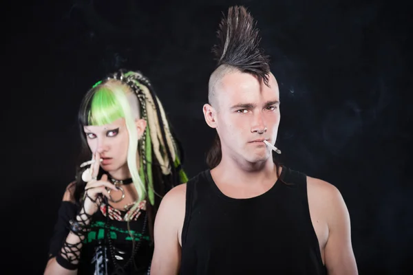 Casal de menina punk cibernético com cabelo loiro verde e homem punk com corte de cabelo mohawk. Caras expressivas. Fumar cigarro. Isolado em fundo preto. Estúdio . — Fotografia de Stock