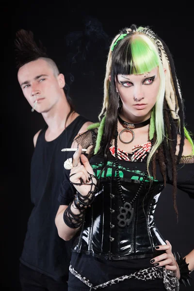Paar von Cyber-Punk-Mädchen mit grün-blonden Haaren und Punk-Mann mit Mohawk-Frisur. Ausdrucksstarke Gesichter. Zigarette rauchend. isoliert auf schwarzem Hintergrund. Studioaufnahme. — Stockfoto