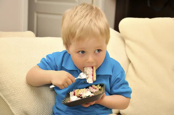 Menino adorável comendo bolo em uma cadeira com um garfo — Fotografia de Stock