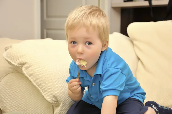 Bedårande pojke äta kakan i en stol med en gaffel — Stockfoto