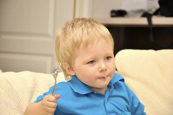 Menino adorável comendo bolo em uma cadeira com um garfo — Fotografia de Stock
