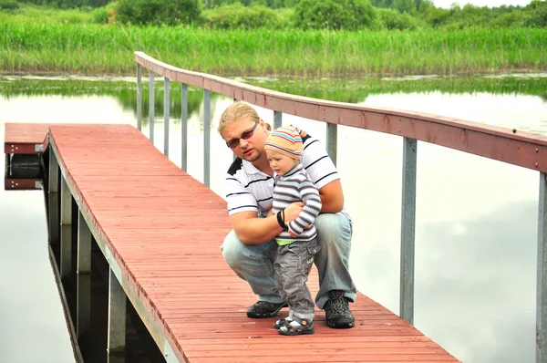 Vater und Sohn auf einem Holzsteg in der Nähe eines Flusses — Stockfoto