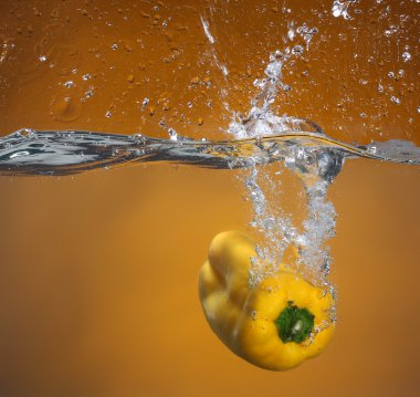 Yellow pepper falling into water. Background in the same tone clipart