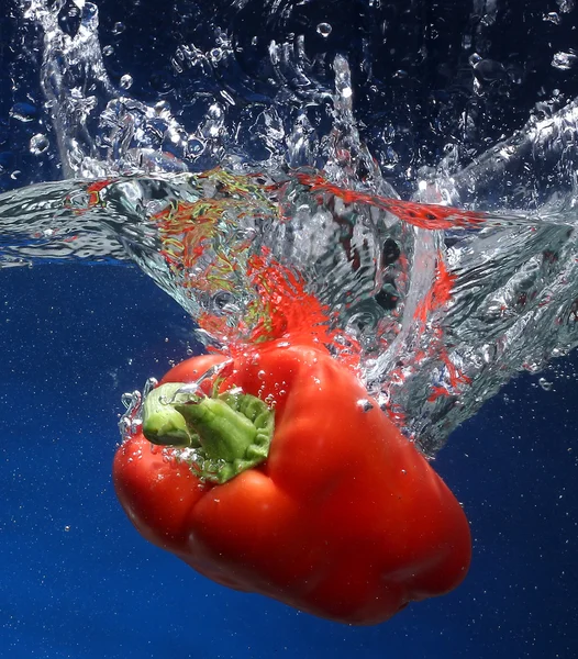 Paprika fällt ins Wasser. blauer Hintergrund — Stockfoto