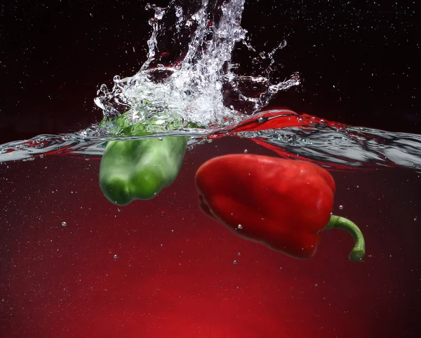 Δύο πιπεριές που εμπίπτουν στο νερό. κόκκινο φόντο — Φωτογραφία Αρχείου