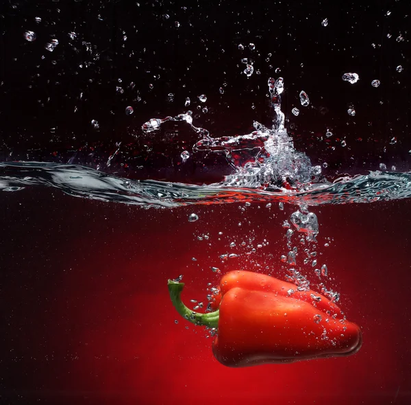 Röd paprika faller i vattnet. bakgrund i samma ton — Stockfoto