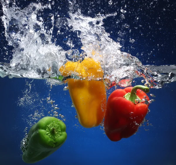 Tre paprika faller i vattnet. blå bakgrund — Stockfoto