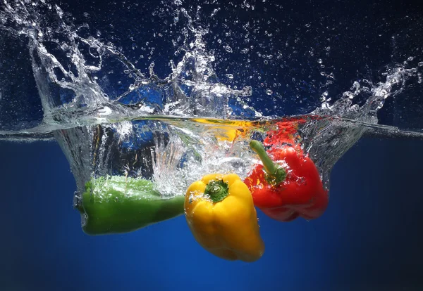 Tři papriky pádu do vody. modré pozadí — Stock fotografie