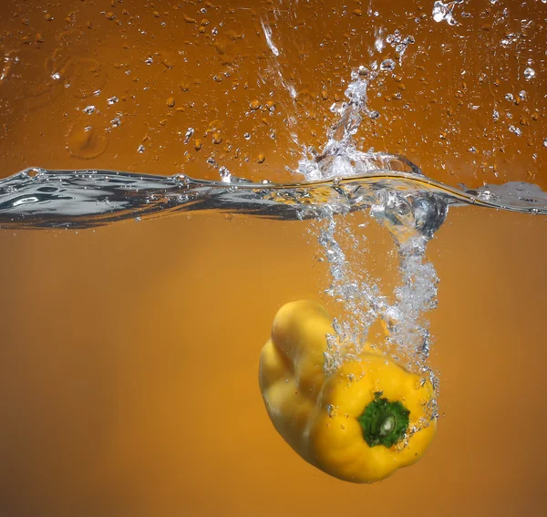 Pimienta amarilla cayendo al agua. Fondo en el mismo tono — Foto de Stock