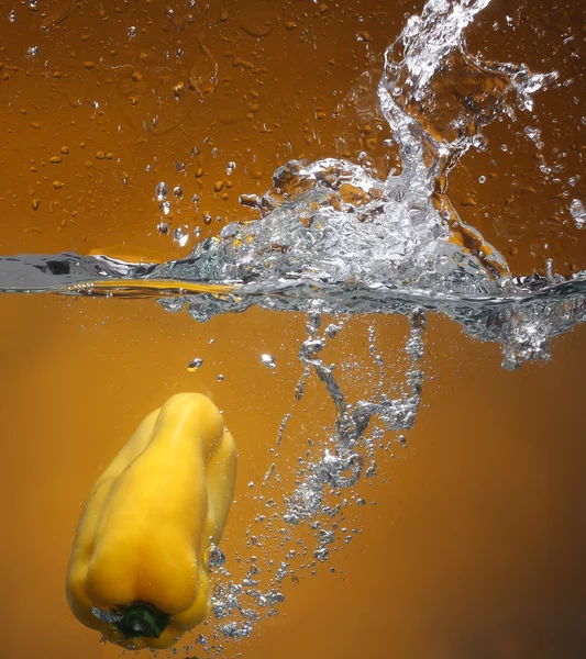 stock image Yellow pepper falling into water. Background in the same tone