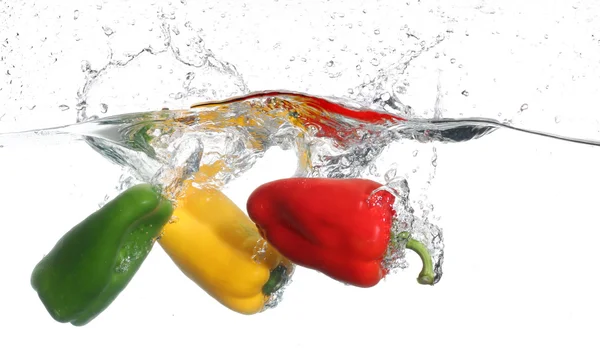 Drei Paprika, die ins Wasser fallen, vor weißem Hintergrund — Stockfoto