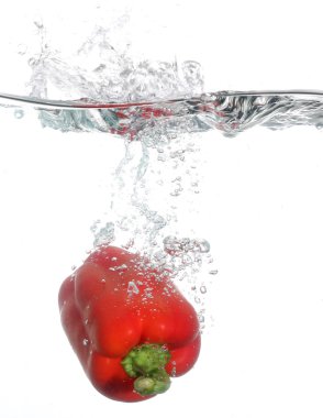 Red pepper falling into water over white background clipart